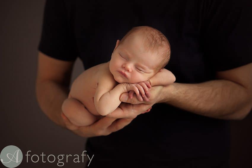 dark background photo of newborn baby girl in dads hands