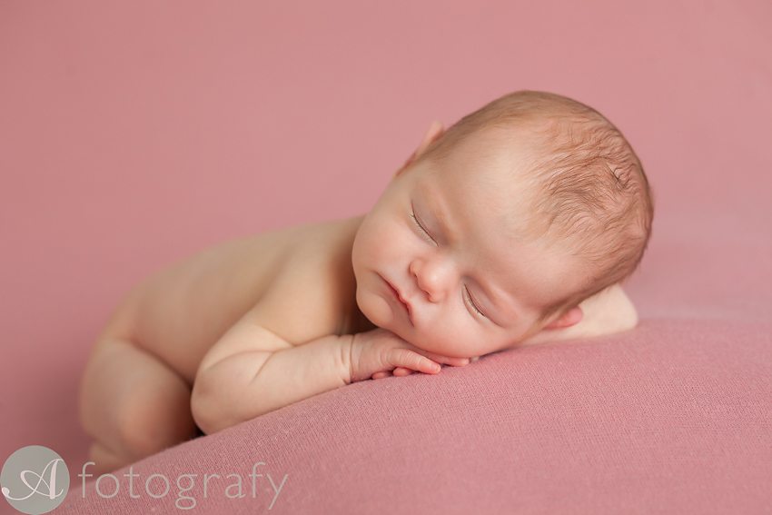 newborn baby photographed in simple side pose on pink blanket