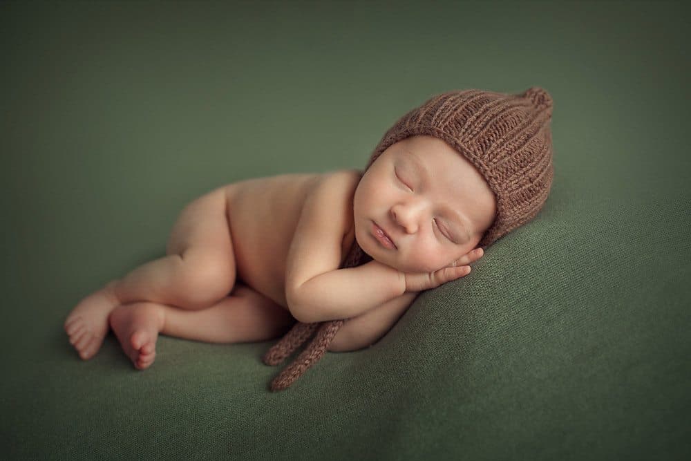 newborn boy on dark green background wearing hat
