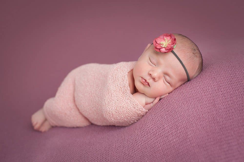 newborn girl wrapped in pink wrap wearing headband during photo shoot