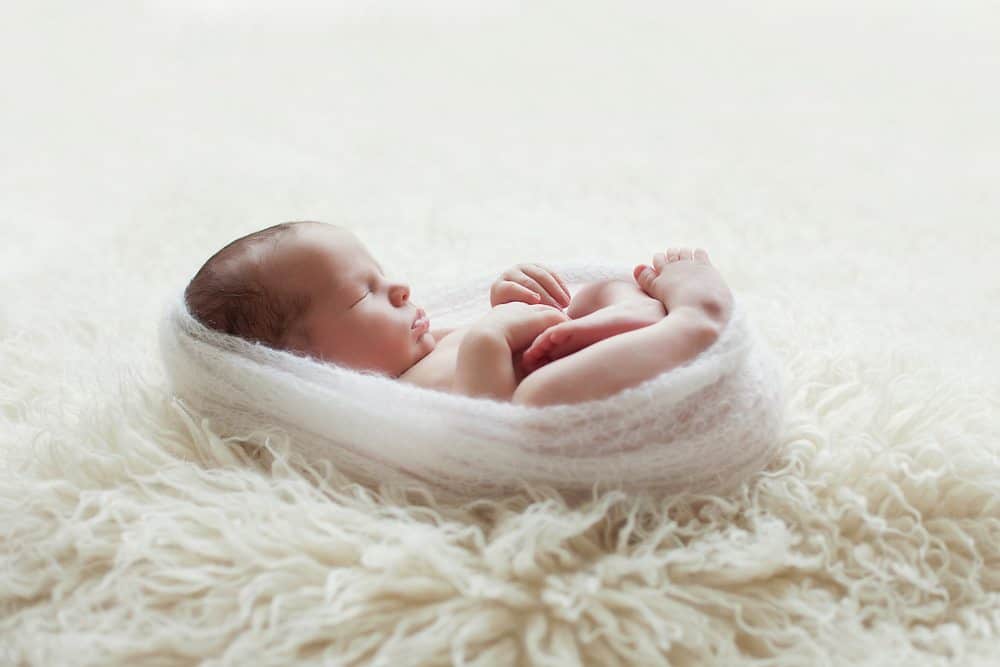 artistic portrait of newborn baby wrapped in light wrap