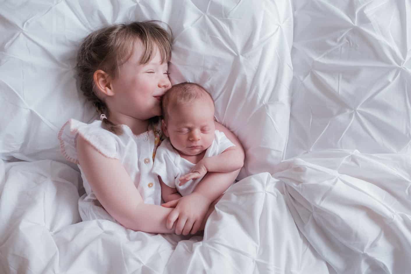 photographer takes newborn baby photoshoot at home with siblings in the bed