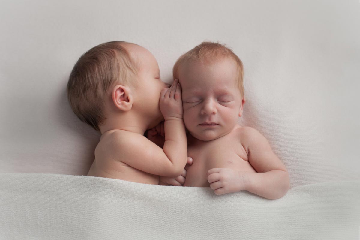 newborn twins holding each other doing a whispering pose. 