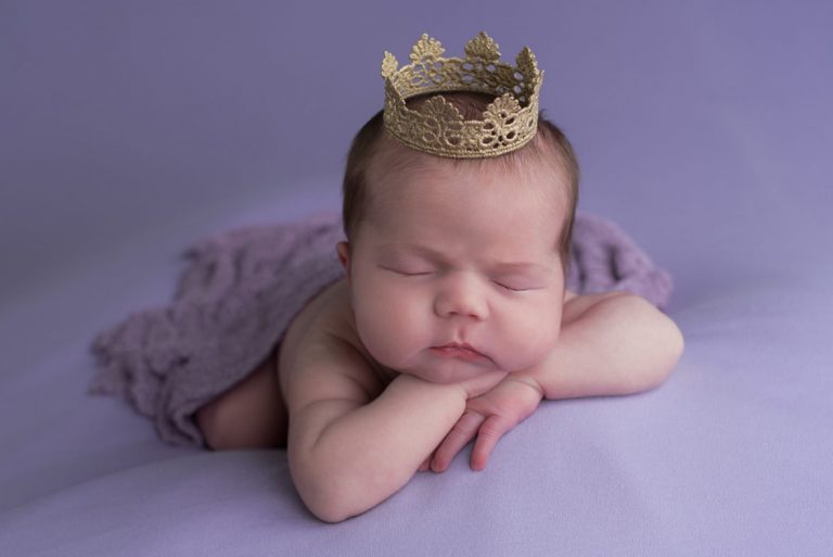 newborn on purple blanket wearing crown during newborn photoshoot